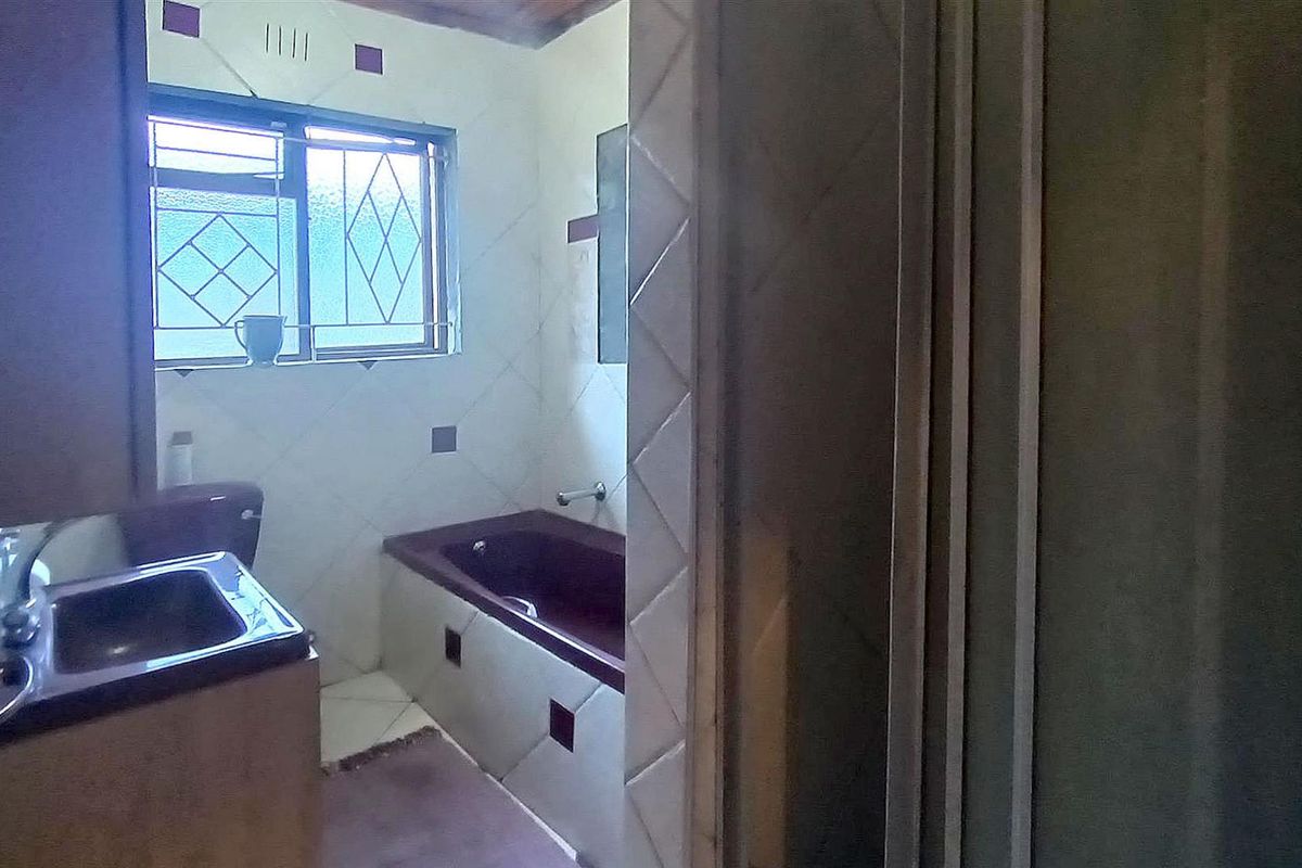 A dated bathroom featuring a built-in bathtub, vanity basin, and tiled walls, requiring modernization to improve its aesthetic and functionality.