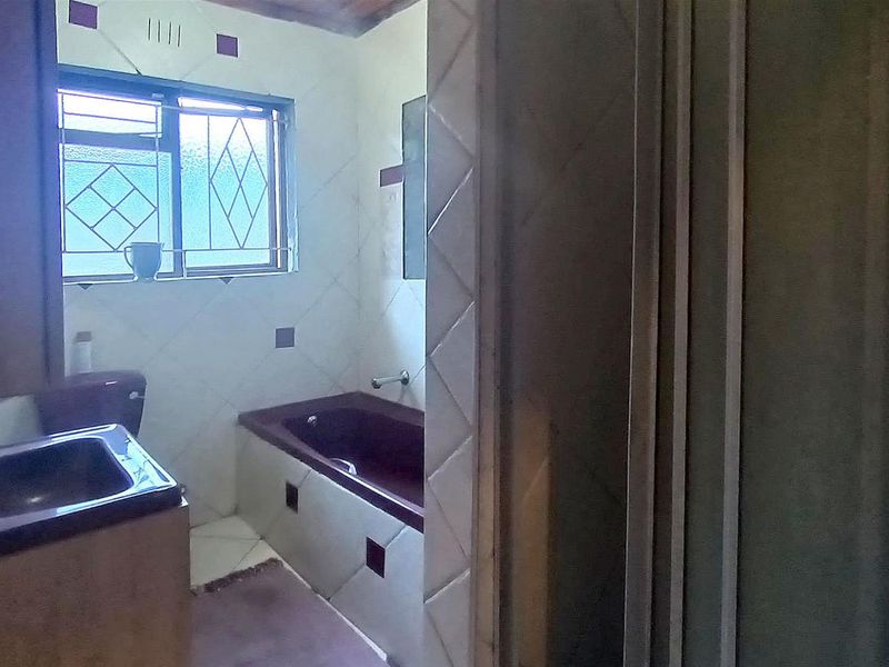 A dated bathroom featuring a built-in bathtub, vanity basin, and tiled walls, requiring modernization to improve its aesthetic and functionality.