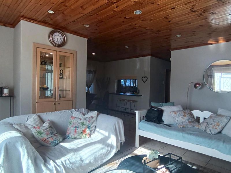 Open-plan living area featuring a timber-clad ceiling, recessed lighting, tiled floors, and a built-in display cabinet, with a view through to the kitchen area.