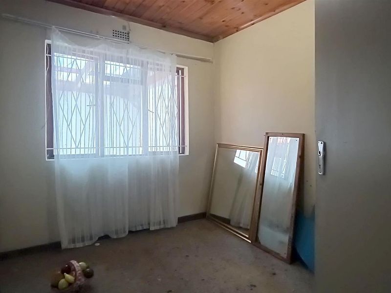 A simple bedroom featuring a timber ceiling and security bars on the window, offering a blank canvas for renovation and interior design updates.