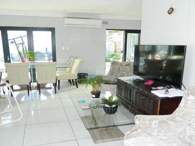 Spacious open-plan living and dining area featuring large aluminium sliding doors, tiled flooring, and a wall-mounted air conditioning unit.