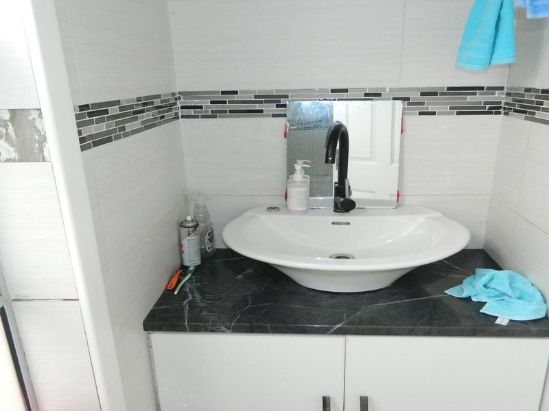 A bathroom vanity area featuring a vessel sink, stone countertop, and mosaic tile accents, currently showing some unfinished wall tiling.