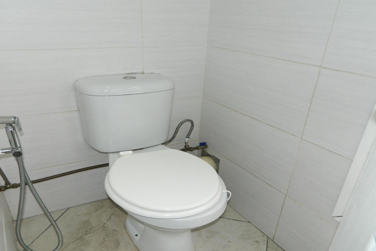 A compact bathroom featuring a standard toilet, bidet spray, and neutral ceramic wall and floor tiling.
