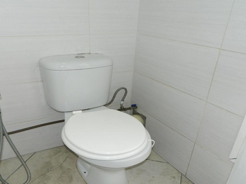 A compact bathroom featuring a standard toilet, bidet spray, and neutral ceramic wall and floor tiling.