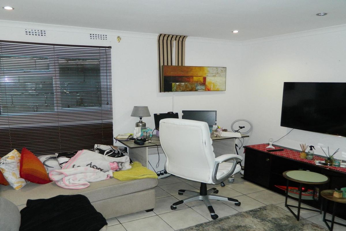 A functional living room featuring tiled flooring, recessed downlighting, and venetian blinds, providing a versatile space for relaxation or home office use.