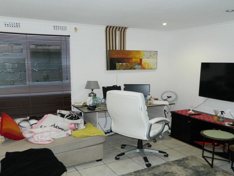 A functional living room featuring tiled flooring, recessed downlighting, and venetian blinds, providing a versatile space for relaxation or home office use.