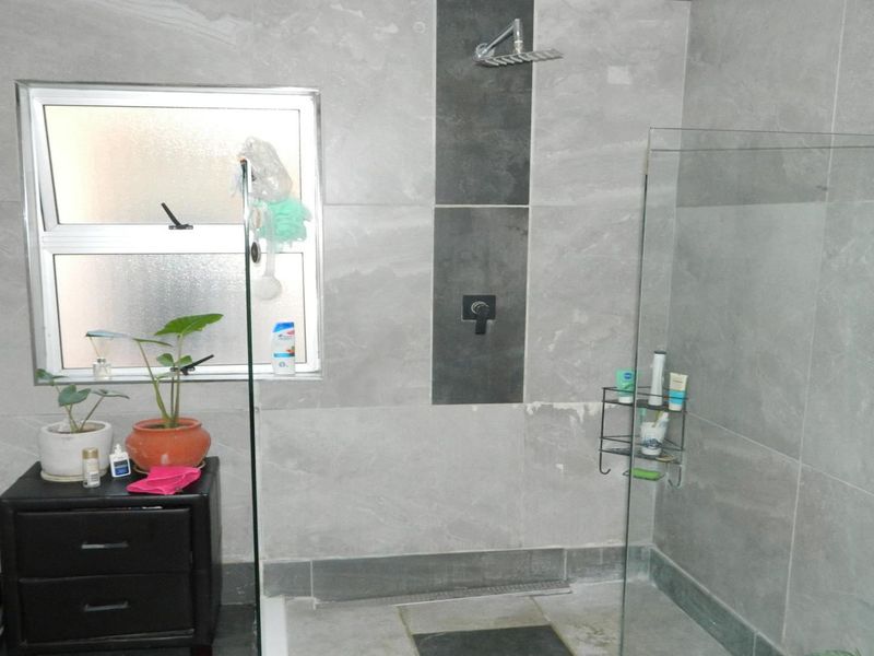 Modern bathroom featuring a walk-in shower with a rain shower head, glass screen, and contemporary grey wall and floor tiling.