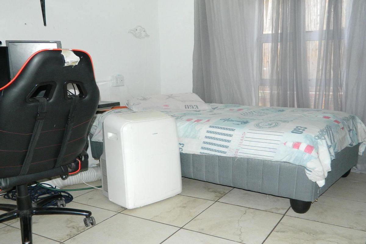 A bedroom featuring tiled flooring and window treatments, currently utilized as a multi-purpose living and workspace.