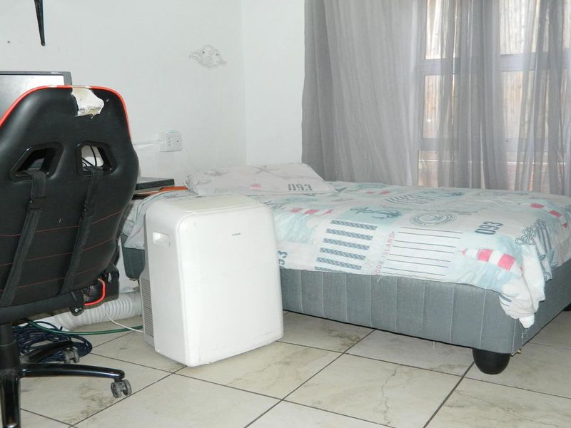 A bedroom featuring tiled flooring and window treatments, currently utilized as a multi-purpose living and workspace.