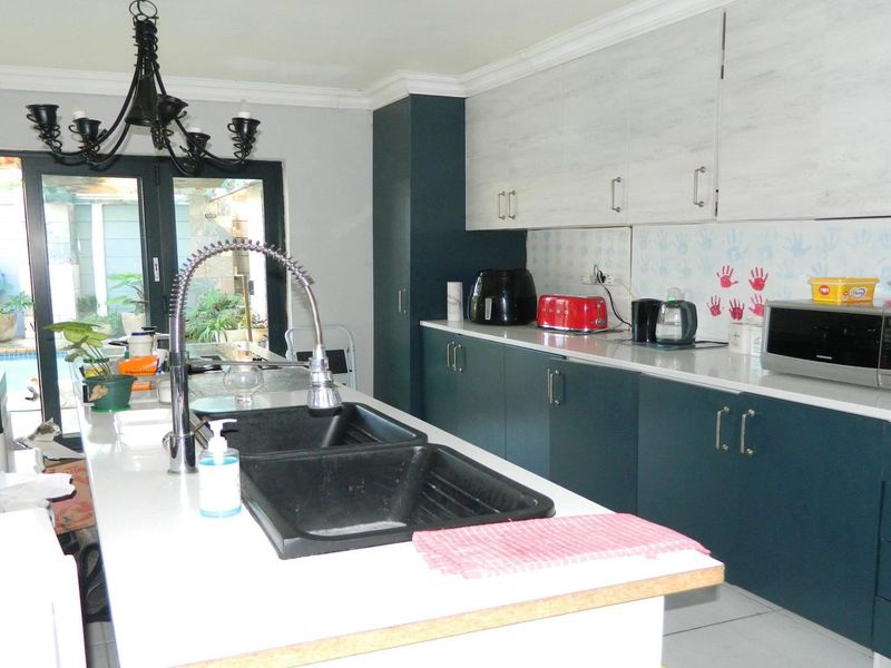Modern kitchen featuring a central island with a double basin sink, stone countertops, two-tone cabinetry, and direct access to the outdoor patio area.