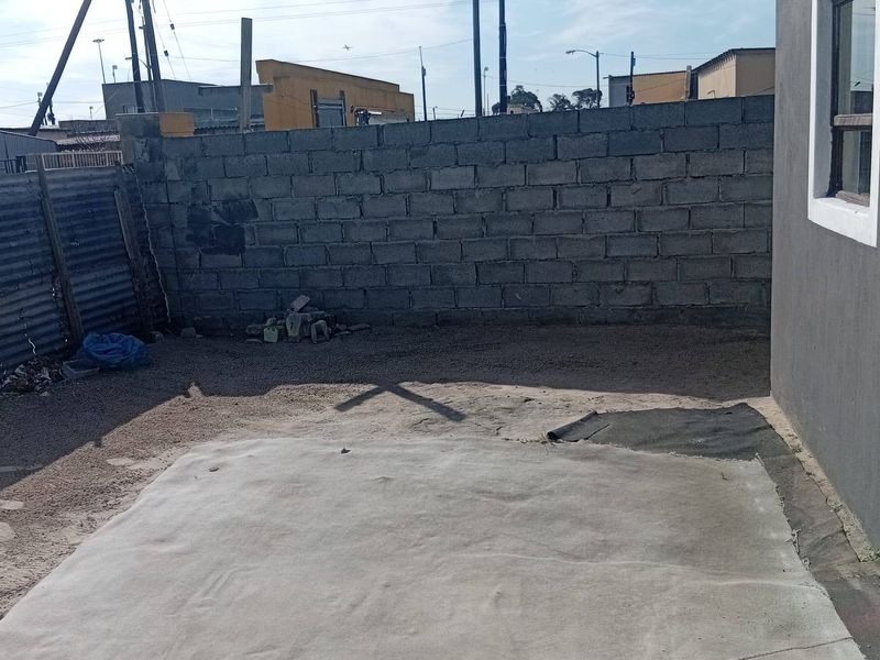A rear exterior area featuring a concrete slab, enclosed by a concrete block boundary wall and corrugated metal fencing.