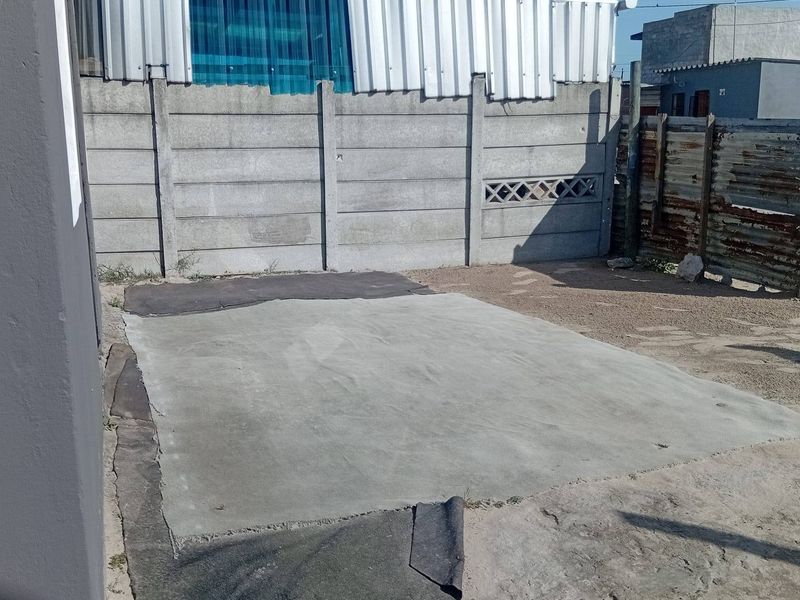 Rear outdoor area featuring a concrete slab, precast boundary walling, and corrugated metal fencing, offering potential for landscaping or patio development.