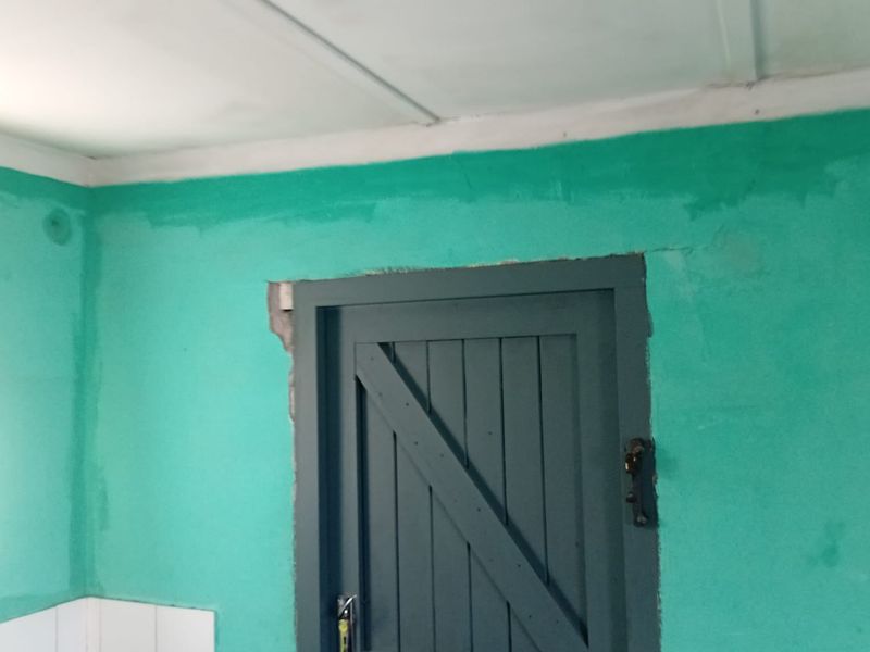 An interior space featuring a timber door and tiled splashback, currently requiring significant cosmetic repairs and repainting to improve the overall condition.