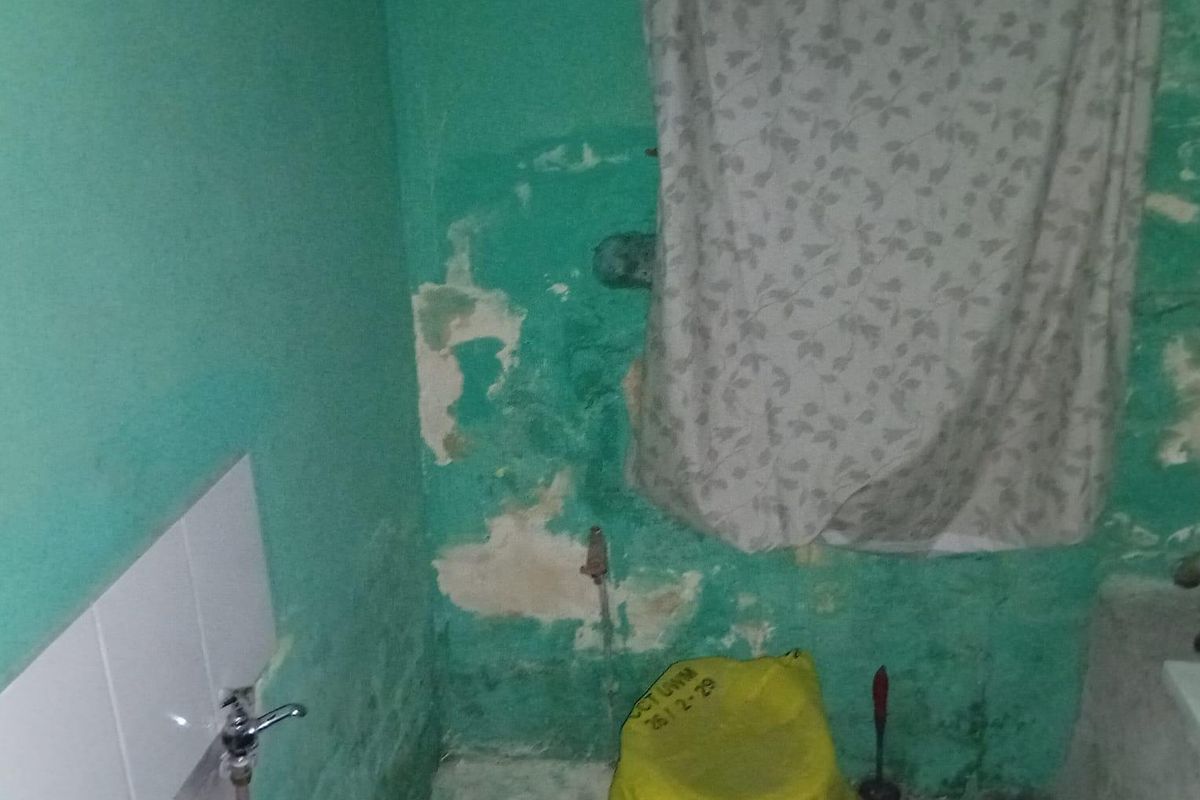A bathroom space requiring significant renovation, featuring damaged wall finishes and basic plumbing fixtures.