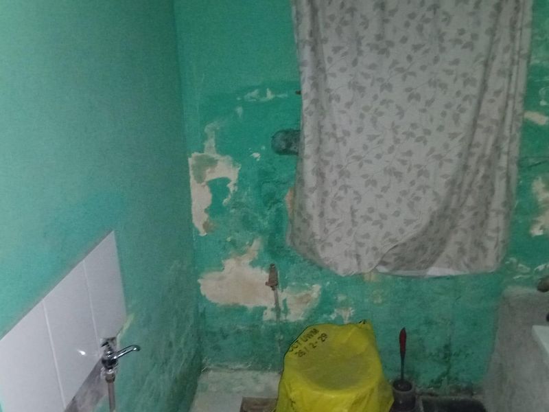 A bathroom space requiring significant renovation, featuring damaged wall finishes and basic plumbing fixtures.