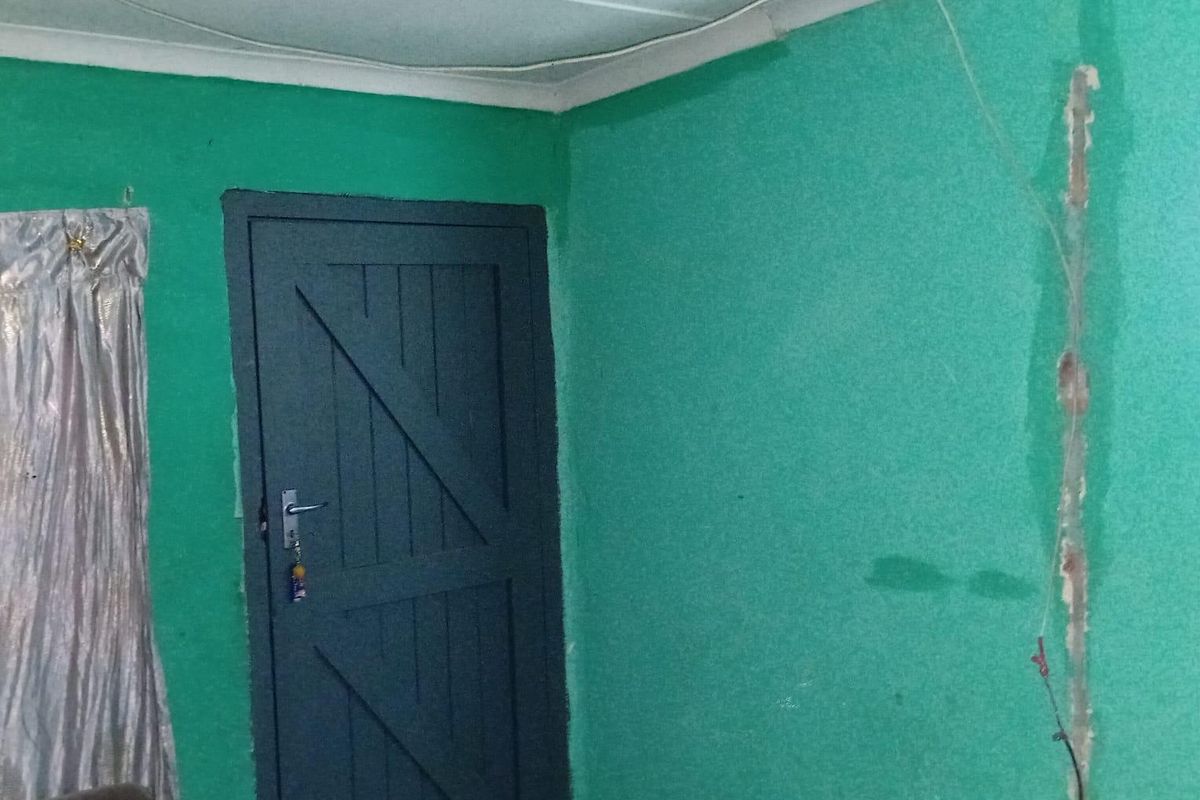 A sparsely furnished living area featuring a timber door and visible wall damage requiring repair and cosmetic updates.