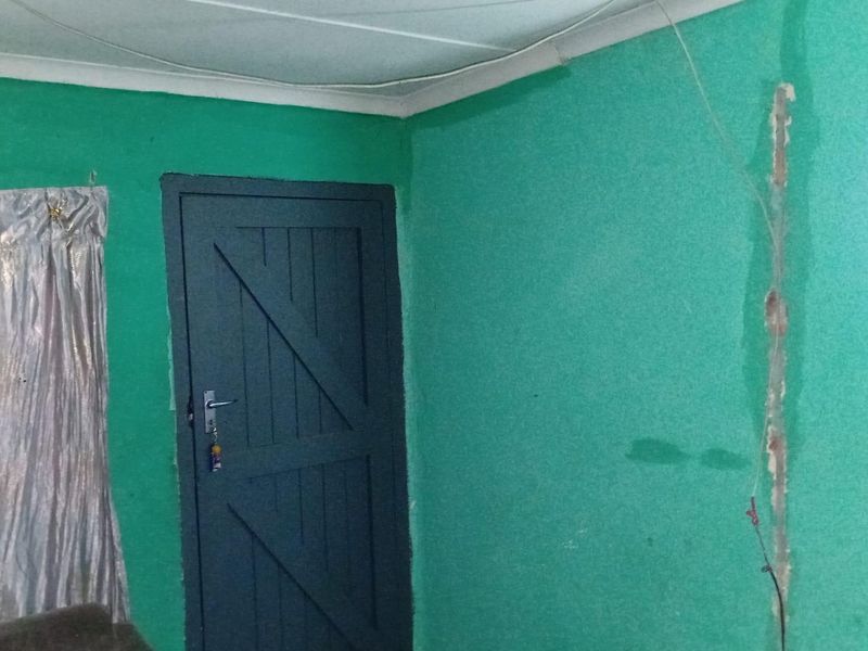 A sparsely furnished living area featuring a timber door and visible wall damage requiring repair and cosmetic updates.