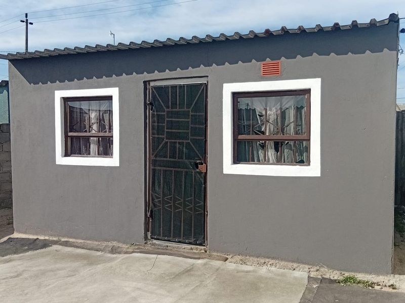 Front elevation of a compact residential structure featuring a security gate, two windows with white trim, and a concrete apron.