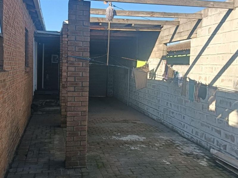 A covered outdoor utility area featuring brick pillars, paved flooring, and exposed timber rafters, suitable for conversion into a functional patio or storage space.
