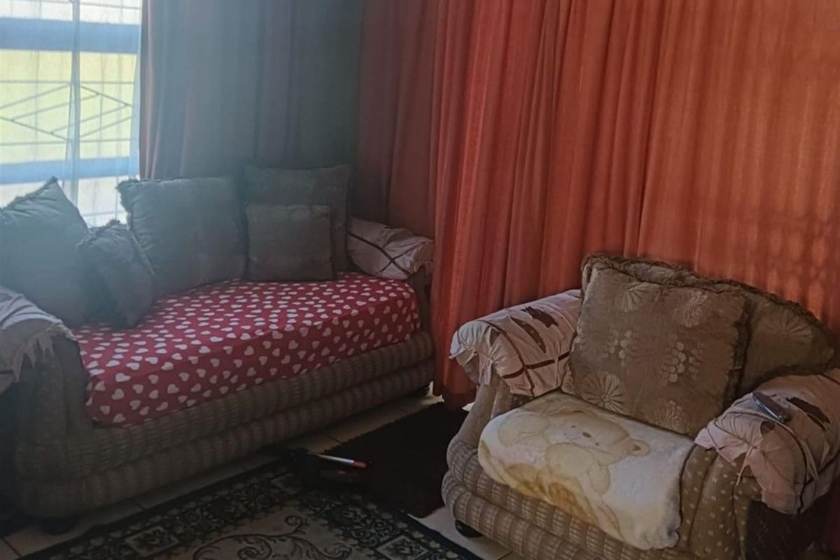 A living room area featuring tiled flooring and large window treatments, providing a functional space for relaxation.
