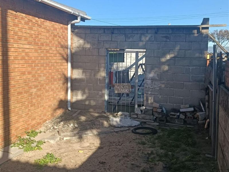 Rear exterior view showing a brick house wall and an unfinished concrete block structure with a metal security gate.