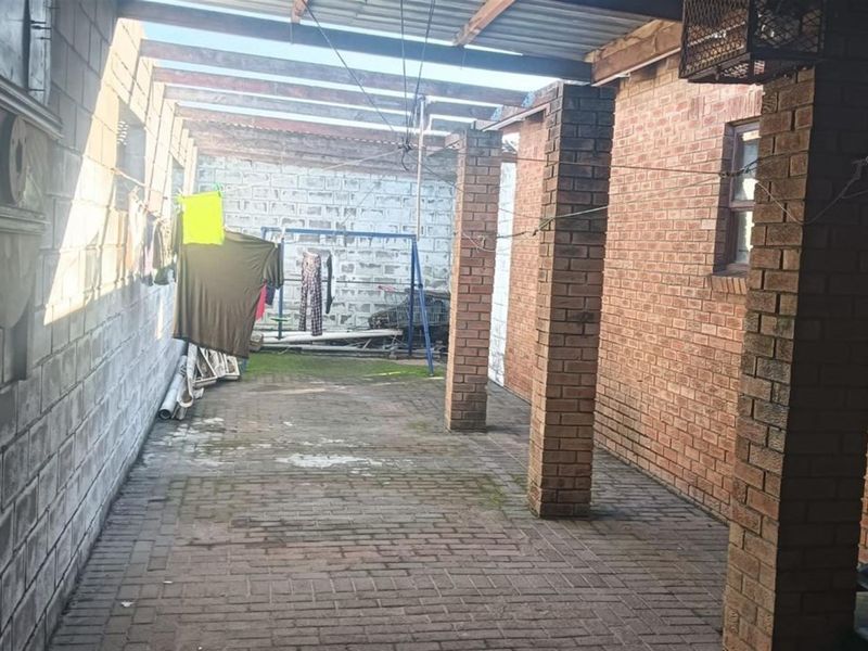 A covered outdoor patio area featuring exposed brick walls, brick pillars, and paved flooring, offering a functional space for outdoor utility or relaxation.