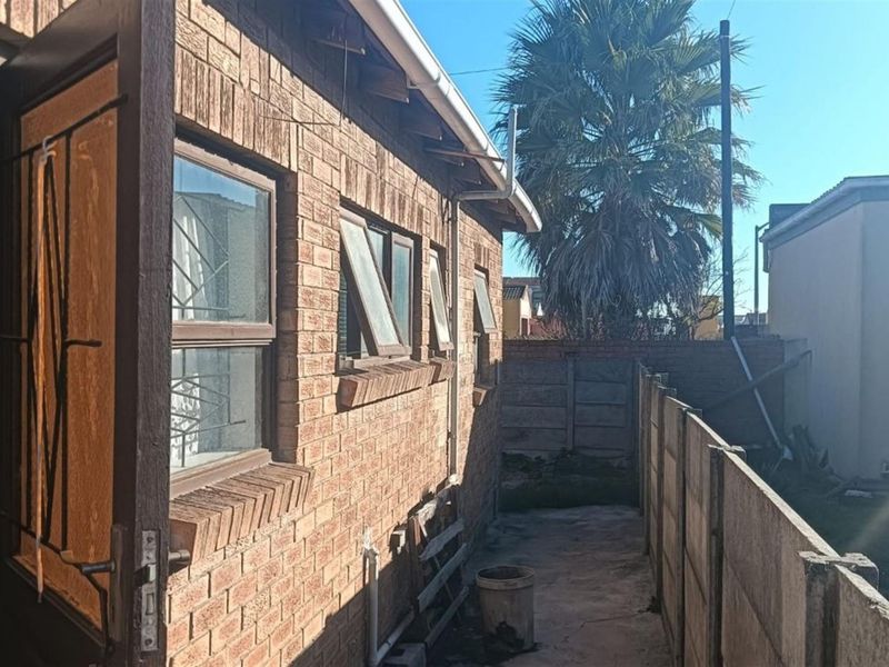 Side view of the property showing face brick exterior, security-fitted windows, and a narrow concrete pathway enclosed by a precast concrete boundary wall.