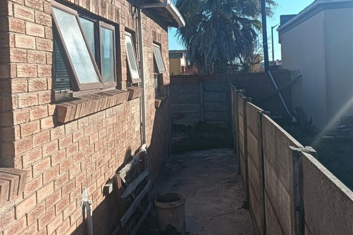 A narrow side passage of the house featuring face brick exterior walls, top-hung windows, and a concrete boundary wall with paved flooring.