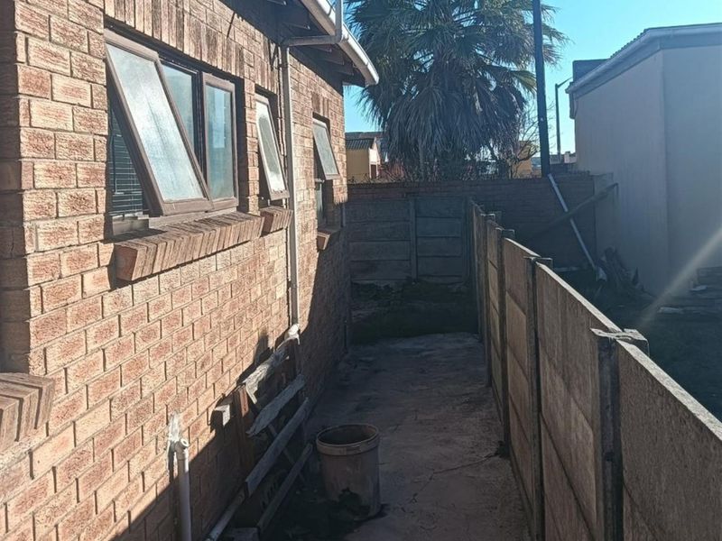 A narrow side passage of the house featuring face brick exterior walls, top-hung windows, and a concrete boundary wall with paved flooring.