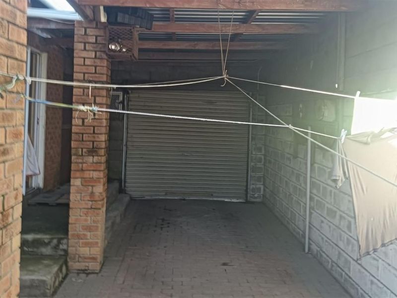 A covered garage area featuring a roller shutter door, brick pillars, and concrete block walls, providing secure parking space.