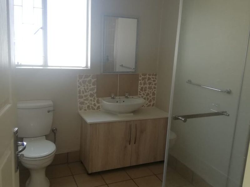 A functional bathroom featuring a vanity cabinet with basin, a toilet, and a glass-enclosed shower with tiled flooring.