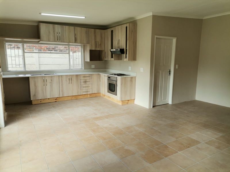 A functional, open-plan kitchen featuring light wood-look cabinetry, built-in oven and hob, and neutral tiled flooring, ready for personalization.