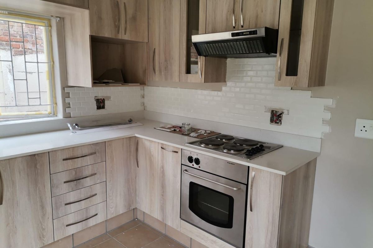 A modern kitchen featuring light wood-grain cabinetry, white countertops, and a subway tile backsplash, currently undergoing final finishing touches and electrical installation.
