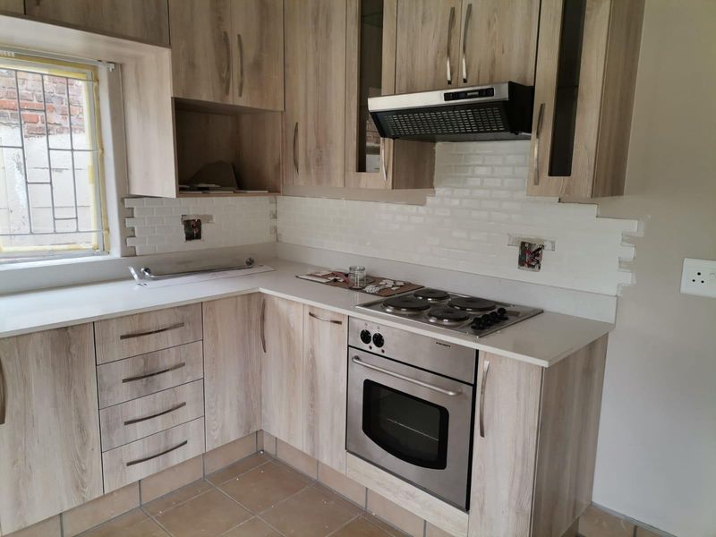 A modern kitchen featuring light wood-grain cabinetry, white countertops, and a subway tile backsplash, currently undergoing final finishing touches and electrical installation.