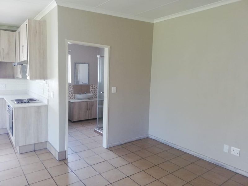 Open plan living area featuring tiled flooring and a modern kitchen with built-in appliances, leading directly into a bathroom.
