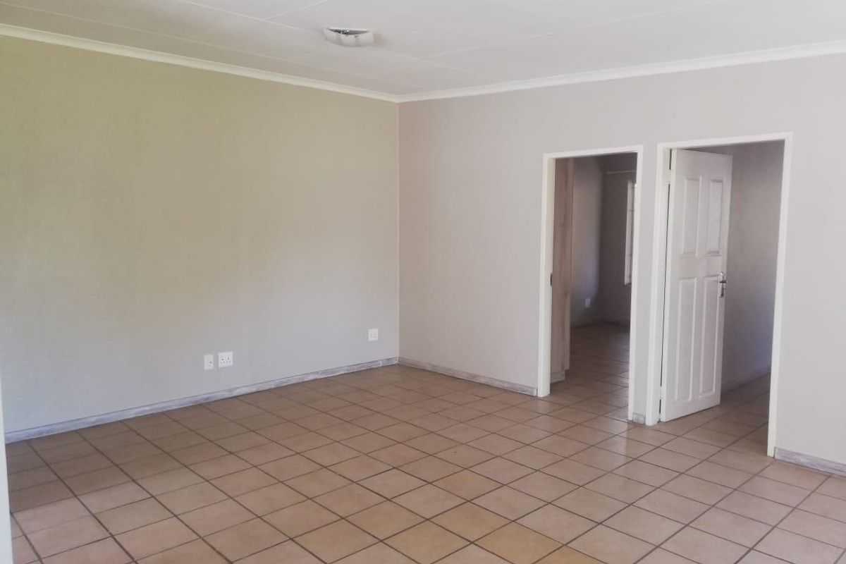 A spacious, empty living area featuring neutral wall paint, ceramic floor tiles, and access to adjacent rooms through internal doors.