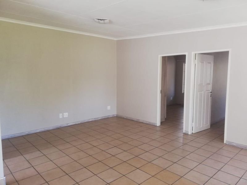A spacious, empty living area featuring neutral wall paint, ceramic floor tiles, and access to adjacent rooms through internal doors.