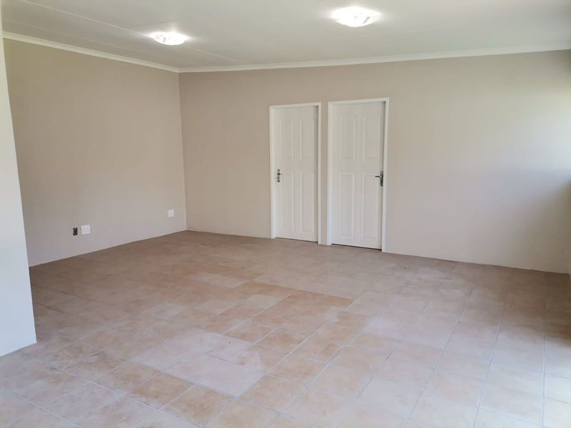 A spacious, empty living area featuring neutral wall paint, tiled flooring, and two interior panel doors.