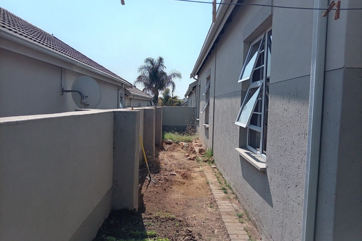 Side passage of the townhouse featuring a boundary wall, casement windows, and an unlandscaped garden area requiring maintenance.