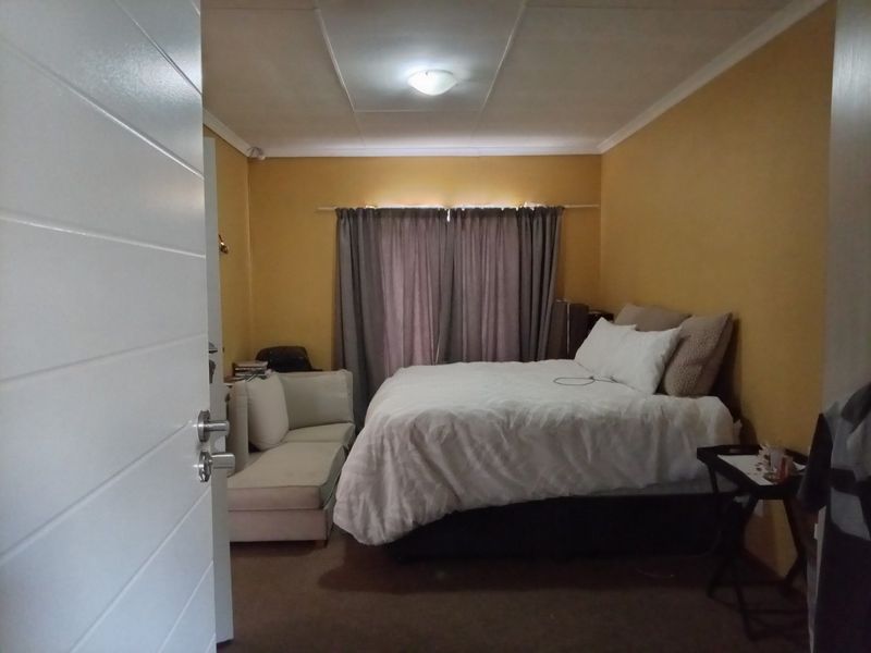 A standard bedroom featuring yellow painted walls, a ceiling light fixture, and a curtain rod over the window area.