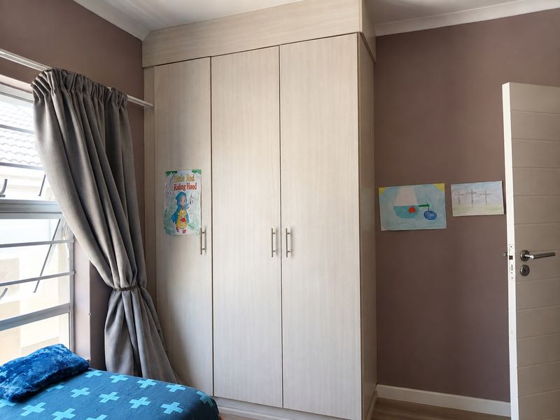 A bedroom featuring a light-toned built-in wardrobe, louver windows, and a modern internal door, finished with neutral wall paint.