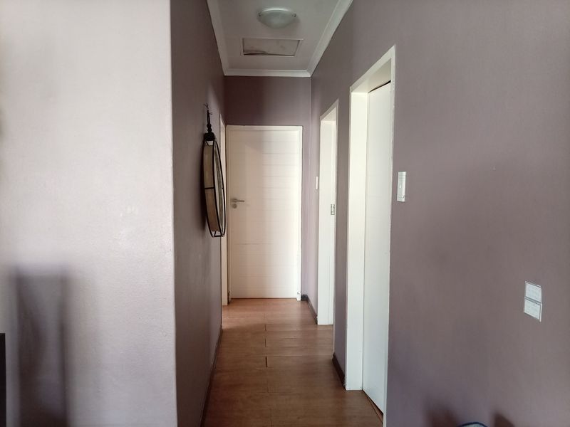 A functional hallway featuring laminate flooring, multiple internal doors, and a ceiling access hatch, providing access to various rooms within the townhouse.