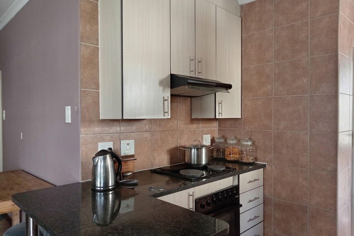 A functional kitchen featuring granite countertops, built-in cabinetry, an electric hob with an extractor fan, and tiled splashback walls.