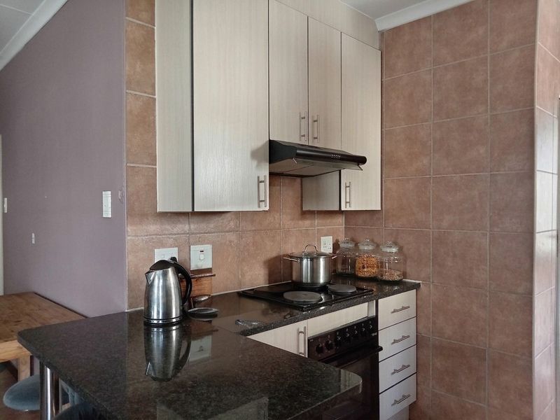 A functional kitchen featuring granite countertops, built-in cabinetry, an electric hob with an extractor fan, and tiled splashback walls.