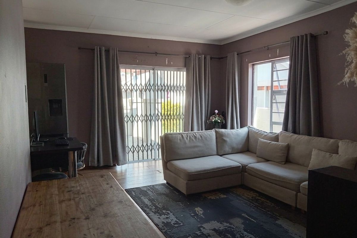 A living room featuring a sliding glass door with security gate, large windows, and neutral wall tones, offering potential for a modern refresh.