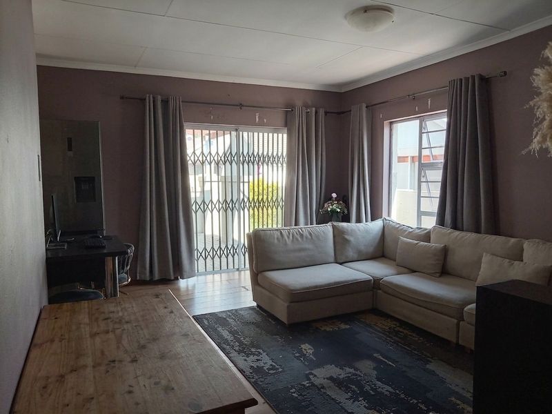 A living room featuring a sliding glass door with security gate, large windows, and neutral wall tones, offering potential for a modern refresh.