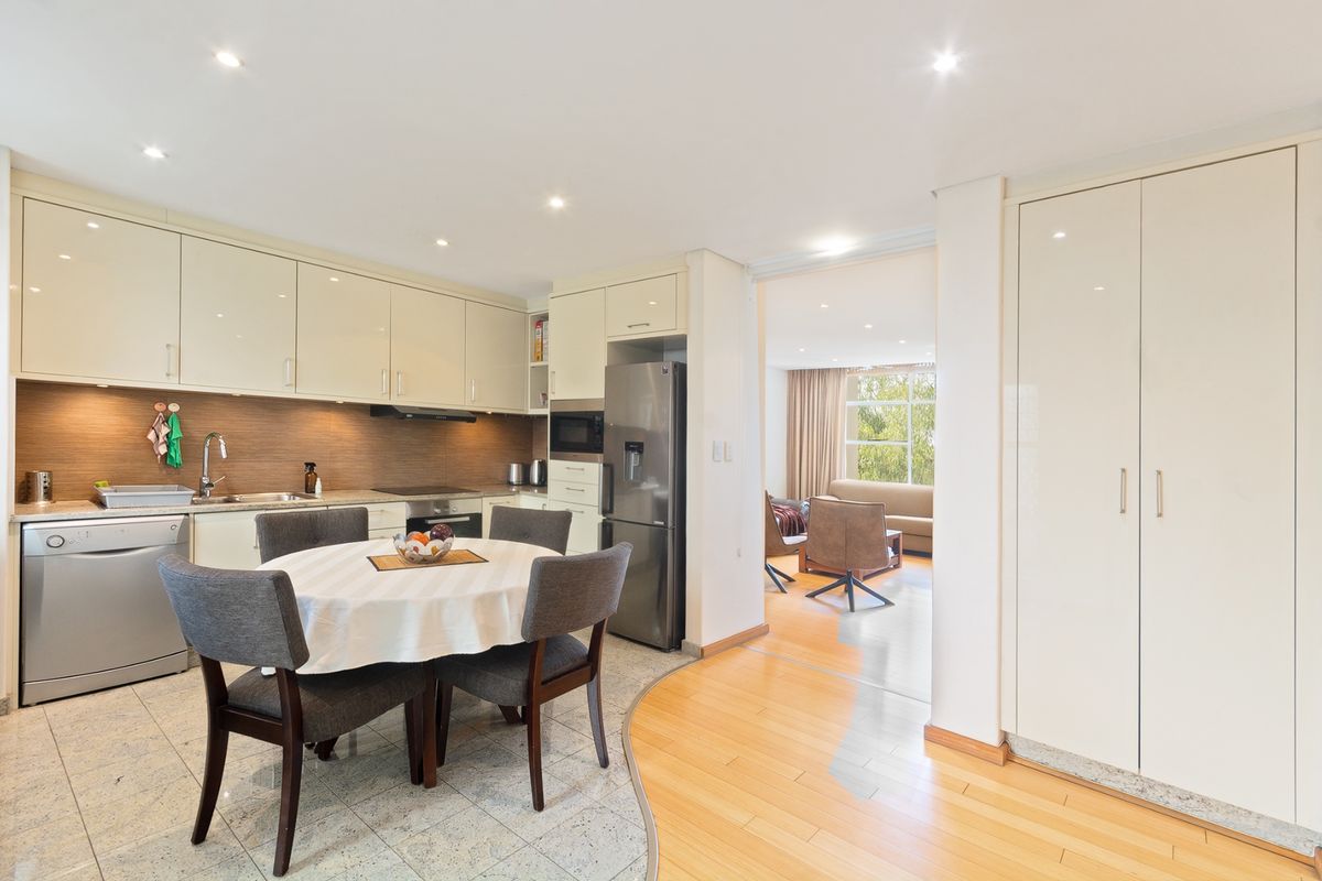 Modern open-plan kitchen and dining area featuring sleek cabinetry, integrated appliances, and a seamless transition between stone and hardwood flooring.