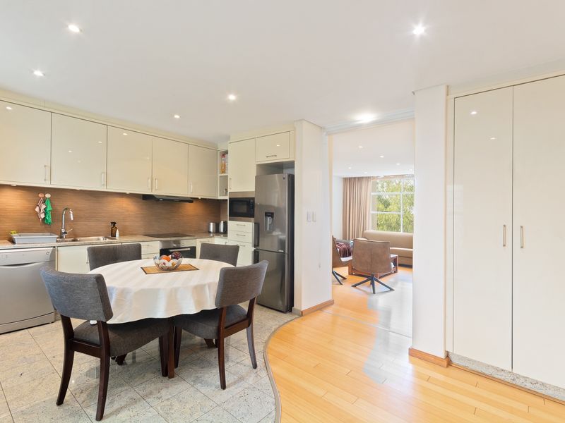Modern open-plan kitchen and dining area featuring sleek cabinetry, integrated appliances, and a seamless transition between stone and hardwood flooring.