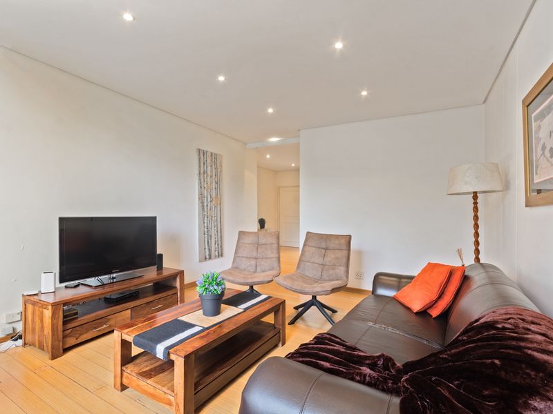 A well-lit living room featuring timber flooring and recessed downlights, providing a comfortable and functional space for relaxation.