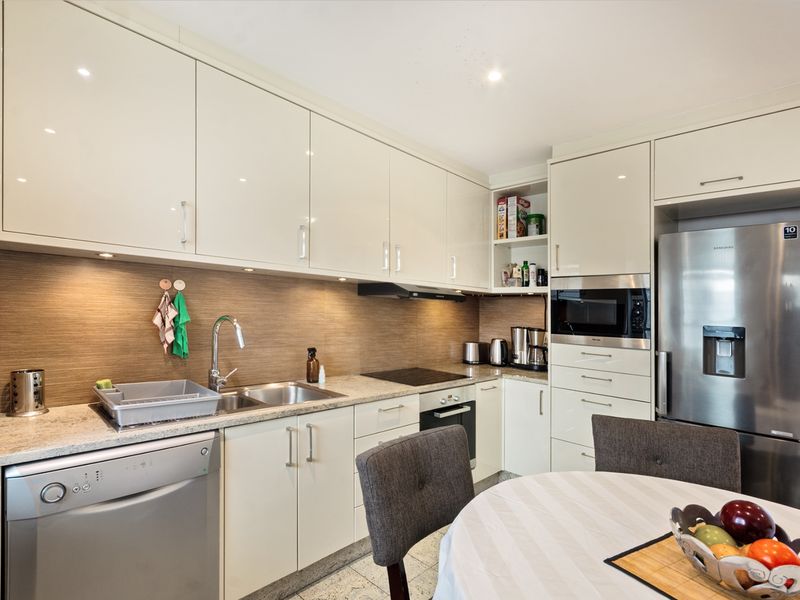 Modern kitchen featuring high-gloss cabinetry, stone countertops, integrated appliances, and a sleek tiled backsplash, offering a clean and functional culinary space.